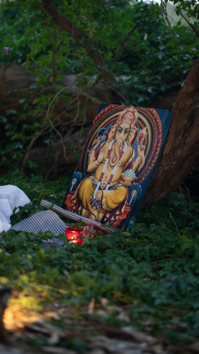 A painted Ganesh image and candle set up in a forest clearing